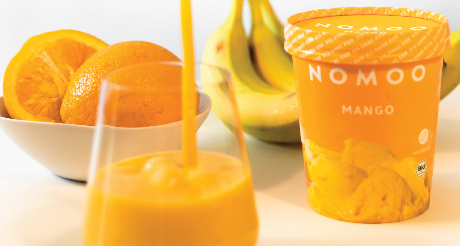 Das Bild zeigt ein Nomoo-Mangoeis sowie eine Obstschale und einen Saft