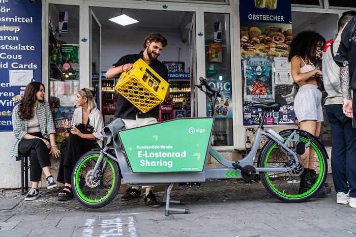 Person mit Getränkekasten befüllt ein Sigo-Lastenrad.