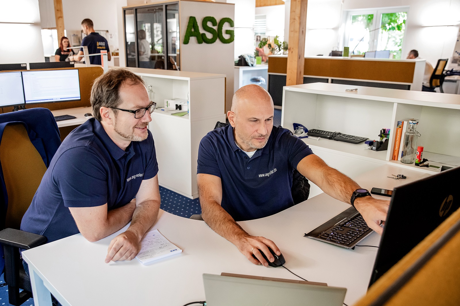 Zwei Mitarbeiter der ASG SolarInvest GmbH sitzen in einem Büro an einem Computer.
