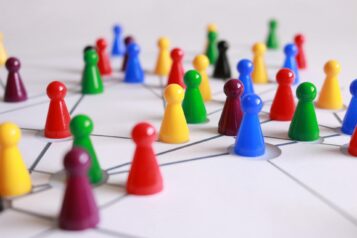Spielfiguren in verschiedenen Farben stehen auf weißem Grund und sind durch Linien verbunden. Das Bild symbolisiert die Beteiligung mehrerer Menschen an einem Projekt.