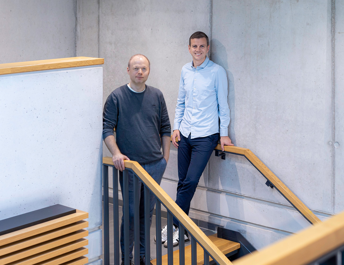 Portrait von Tim Ohm und Maik Bernstein, sie stehen locker im Treppenhaus und lächeln