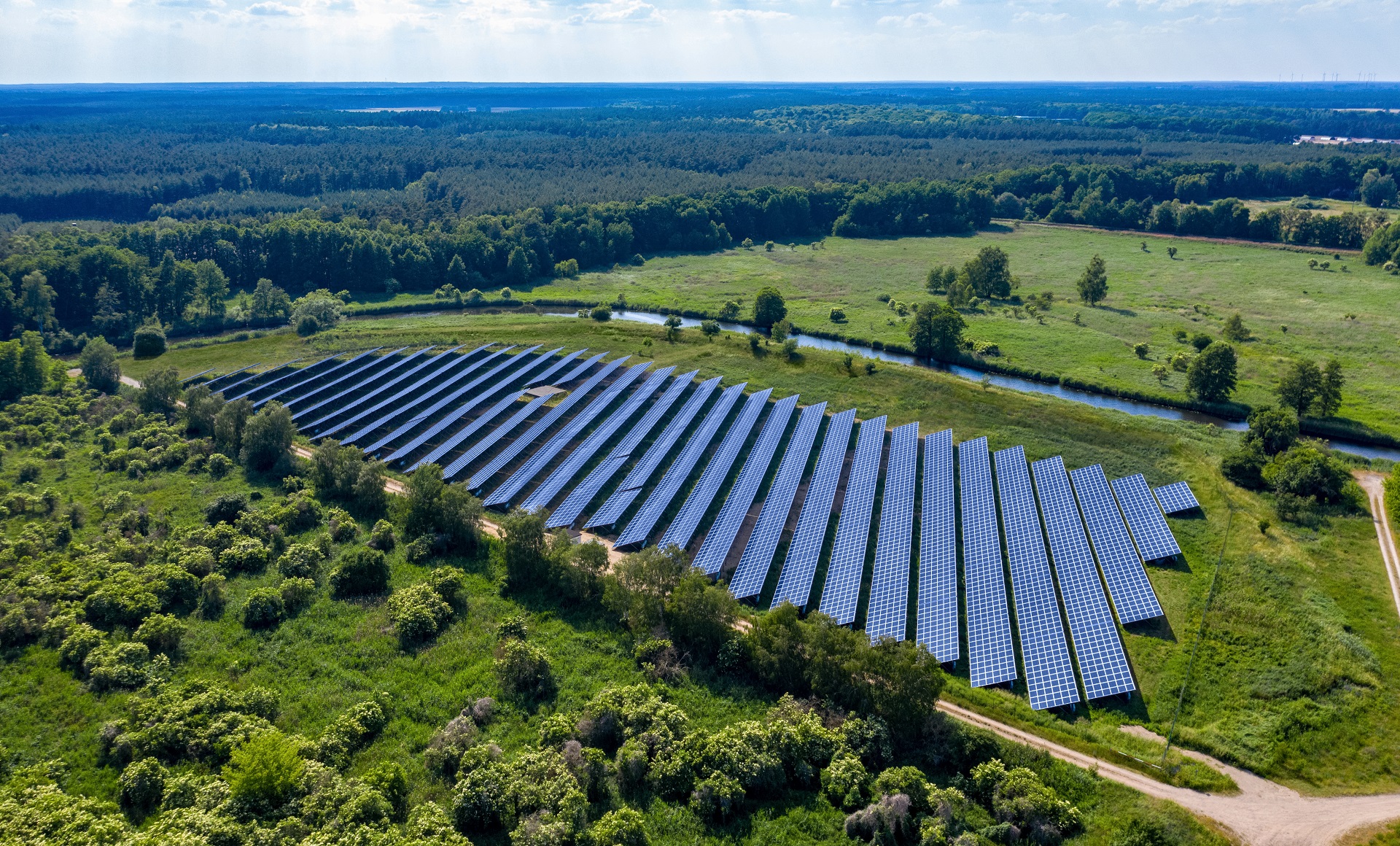 Luftaufnahme eines Solarparks der Consilium Gruppe mit Solarmodulen auf einer grünen Wiese, umgeben von Bäumen und Landschaft.