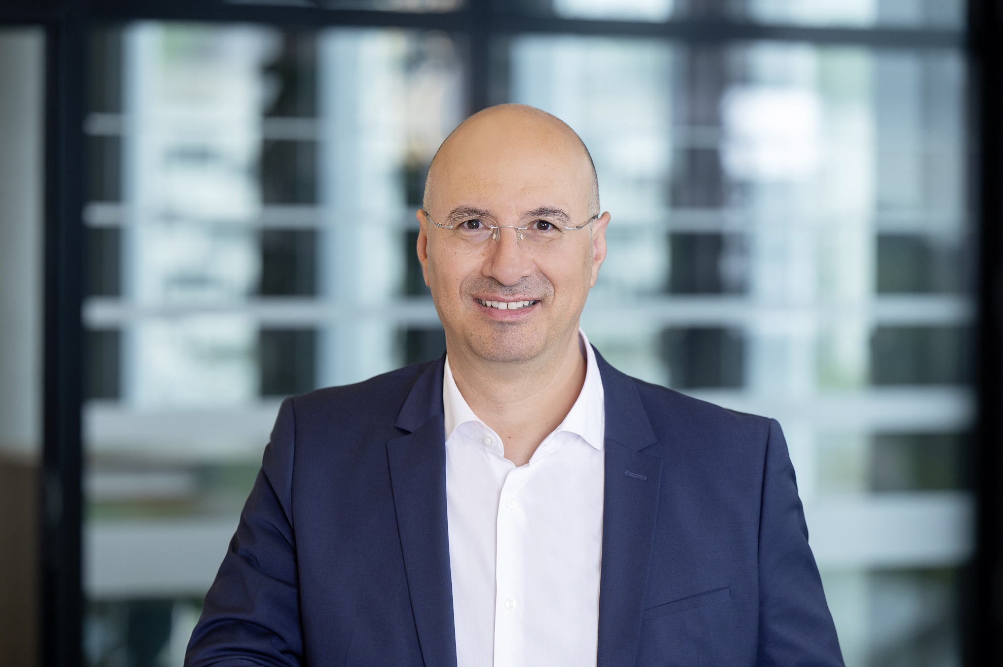 Erol Kiris, Geschäftsführer der Consilium Project Finance GmbH steht im Anzug mit weißem Hemd vor einem modernen, lichtdurchfluteten Bürogebäude.