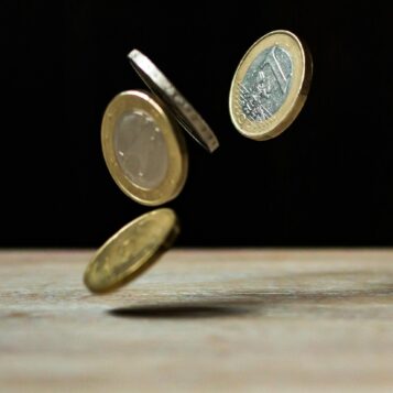 Vier Ein-Euro-Münzen fallen auf einen Tisch vor schwarzem Hintergrund.