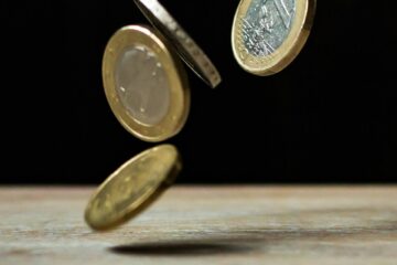 Vier Ein-Euro-Münzen fallen auf einen Tisch vor schwarzem Hintergrund.